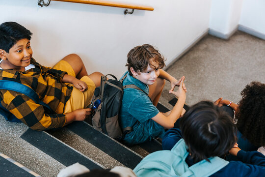 High angle view of boys sitting and talking with friends on steps in elementary school