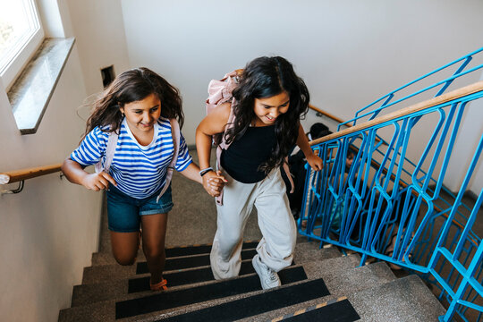 High angle view of cheerful female friends running on stairs of school building