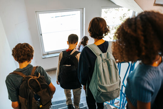 Rear view of male and female students moving down stairs of school building