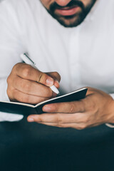 Cropped image of male journalist writing notes in personal planner creating ideas for public article during remote job in coworking space, selective focus on textbook for publication text or checklist