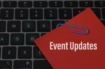The image depicts a keyboard with a red sticky note attached to it, containing the words "Event Updates."