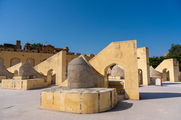 the unique astronomical instruments at Jaipur’s Jantar Mantar observatory. The geometric structures, made of yellow sandstone, feature arches and curves under a bright sunlit sky.