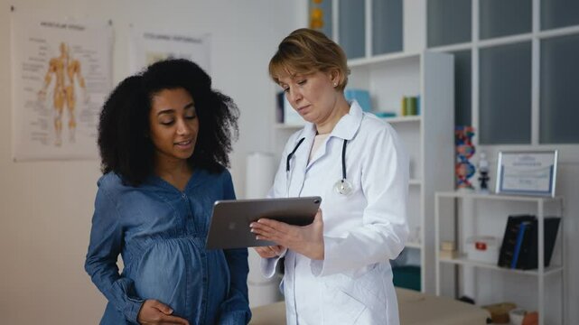 Obstetrician showing baby ultrasound image to pregnant young woman in clinic