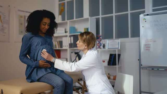 Female doctor examining pregnant woman's belly, listening to fetal heart rate
