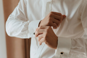 A man is getting dressed in a white shirt and is adjusting his cuff. Concept of formality and attention to detail, as the man takes care to properly dress himself