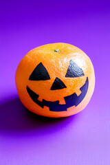 tangerine colored with black paint as jack o lantern, healthy Halloween snack concept. Isolated on solid purple background