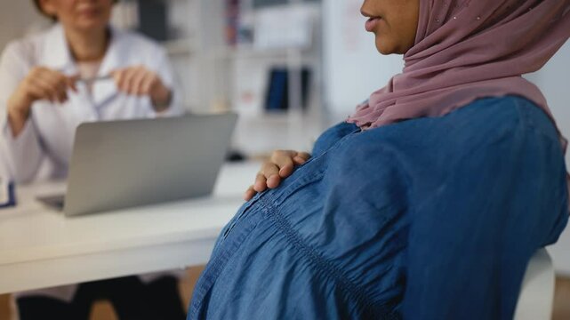 Pregnant Muslim woman talking to obstetrician during clinic check-up, health