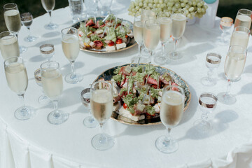 A table with a white tablecloth and a variety of food and drinks, including wine glasses and champagne flutes
