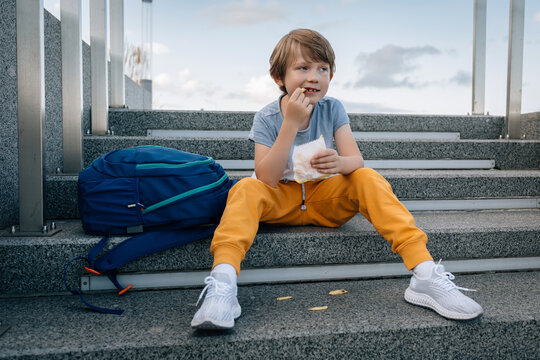 Little boy, with backpack, eats street food, French fries