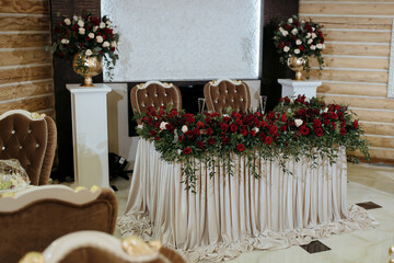 A table with a white tablecloth and red flowers on it. The table is set for a wedding reception