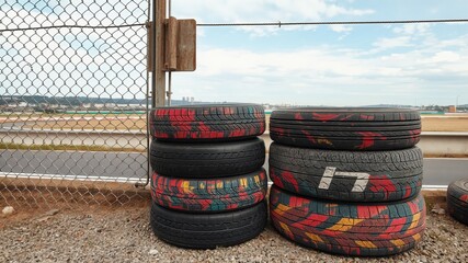 A neat stack of racing tires, varicolored and worn, lies next to the track, surrounded by chain-link fencing,