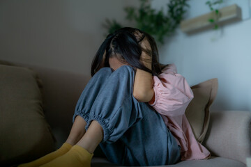 Asian depression teenager covering her face feeling anxious and unhappy. Young woman girl sit on sofa in living room with sad emotional alone, and have mental disorders in house. Mental health concept