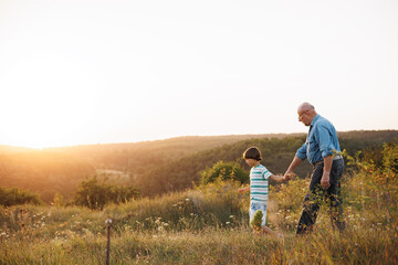 Photo of a little boy with his grandfather walking in a field at summer