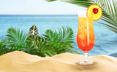 Summer beach with delicious Tequila Sunrise cocktail, tropical leaves and golden sand, space for text