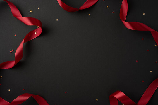 A stylish composition featuring a red ribbon and scattered star confetti on a smooth black background, perfect for festive occasions and celebrations