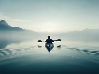 A person kayaking on a calm lake surrounded by misty mountains at dawn.