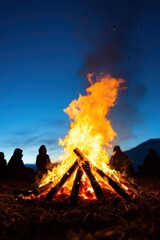 Campfire glowing in the night, surrounded by silhouettes of people.