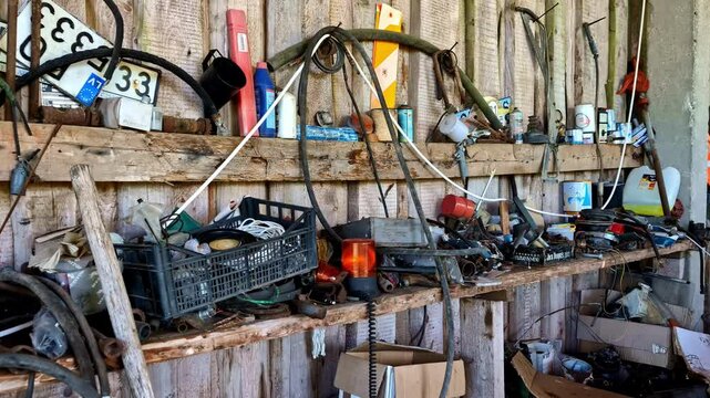A cluttered workshop shelf filled with tools, parts, and miscellaneous items in an old barn