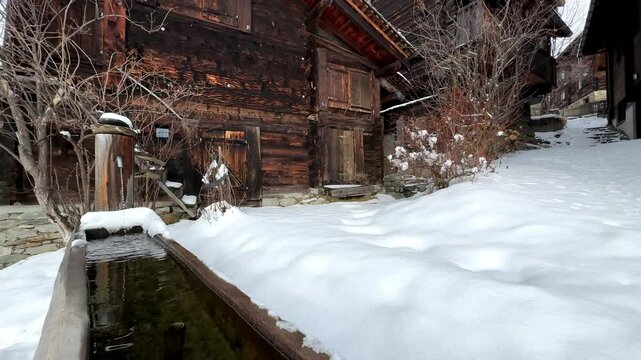 Relaxing winter scene of an old mountain village in Switzerland with huts and a fountain in the snow
