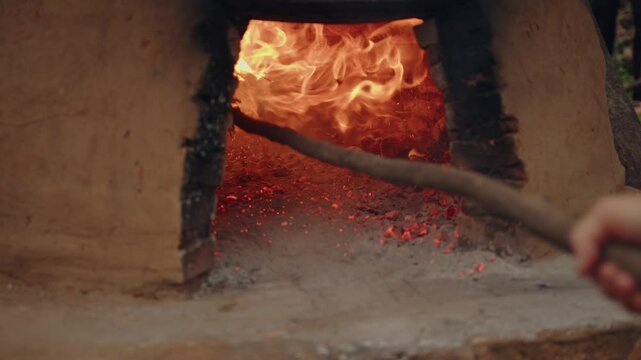 A woman cleaning inside a tatakua with a broom that catches fire due to the intense heat. The tatakua is a traditional clay oven from Paraguay