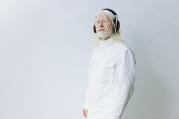 elderly man with long white hair and headphones, dressed in a stylish white outfit, standing against a minimalistic light background Stylish and modern appearance, conveying calm and creativity