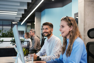 Portrait of call center worker accompanied by his team. Smiling customer support operator at work.