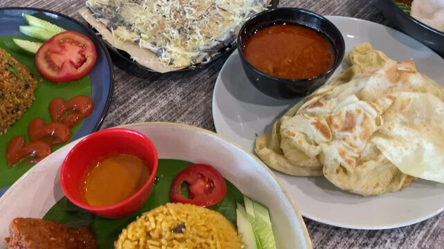 Variety of Malaysian food in the dishes. Fried rice, curry canai, chocolate canai, and fried noodle on the restaurant table.