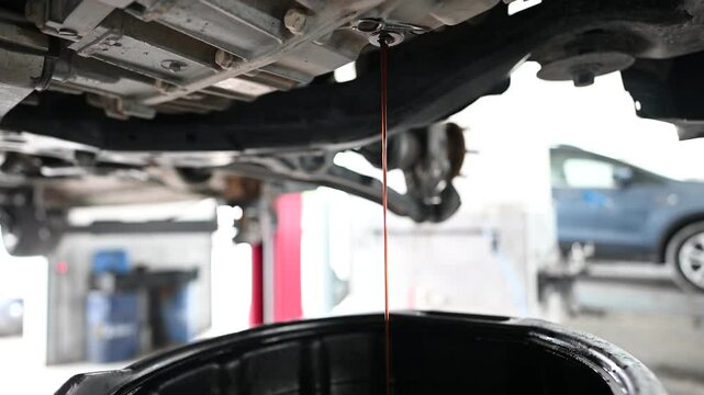 Used engine oil drains from a car engine into a pan. Car maintenance and repair, oil change service concept. Close up.