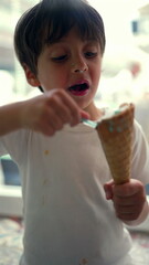 Young boy savoring ice cream with focused attention, using a spoon to enjoy the treat from a cone, capturing a simple and joyful childhood moment indoors