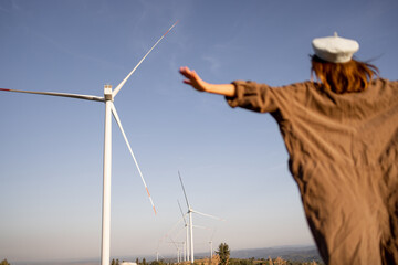 Person with outstretched arms embracing the power of wind energy, standing in front of large wind turbines, symbolizing renewable energy and sustainability