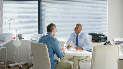 Obraz premium Mature Male Patient Sitting At Desk Having Consultation With Doctor In Office