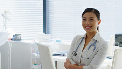 Portrait Of Smiling Female Doctor With Stethoscope Standing By Desk In Office Or Surgery