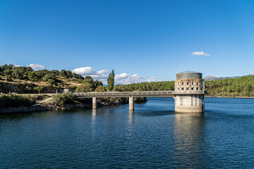 Reservoir maintenance building and walkway over the water, surrounded by forested hills and blue skies