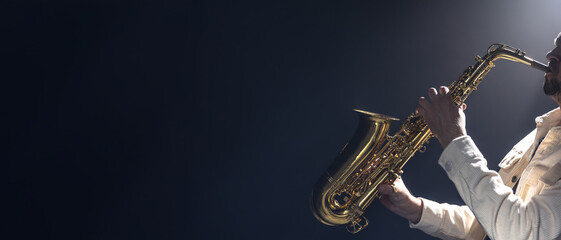 A young man plays the saxophone. Saxophonist on a dark background.