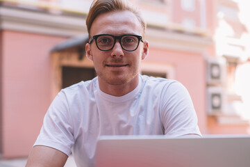 Portrait of skilled male IT professional in stylish eyewear looking at camera during break from online programming and initializing data system, successful man spending time for creating article