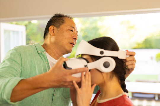 Adjusting VR headset, father helping girl experience virtual reality at home - Powered by Adobe
