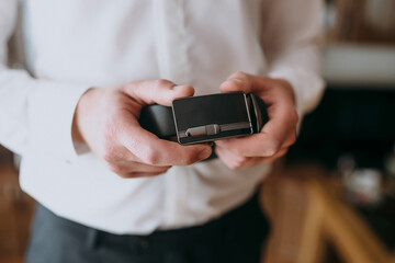 A man is holding a belt with a silver buckle. The buckle is engraved with a design that looks like a cross. The man is wearing a white shirt and black pants