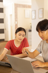 Using laptop, young asian brother and sister discussing work  at home desk