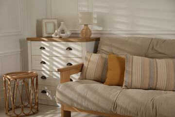 Sofa with soft pillows, chest of drawers, different decorative elements and side table indoors