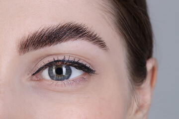 Woman after brow lamination procedure on grey background, closeup