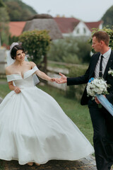 A bride and groom are walking down a path with a white dress and a blue tie. The bride is holding the groom's hand