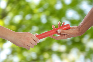 Man passing relay baton to teammate outdoors, closeup