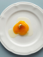 Still life with raw egg and a gold ring on a white plate on pastel blue background. Minimal and creative jewelry photography concept