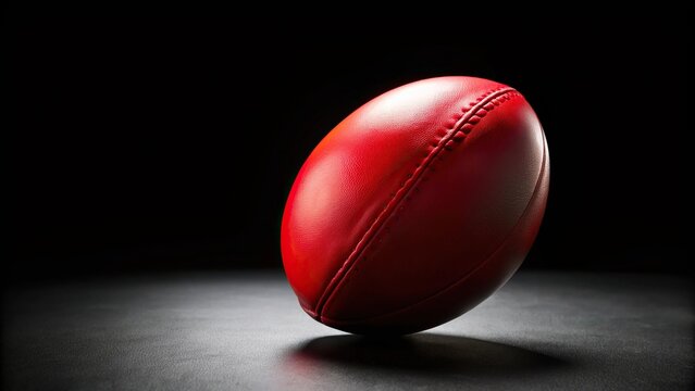A close-up shot of a red Australian rules football on a black background with selective focus
