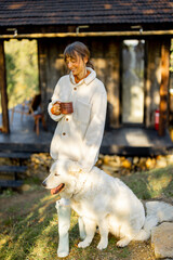 A woman in a cozy fleece jacket enjoys her morning coffee outdoors, standing next to her friendly...