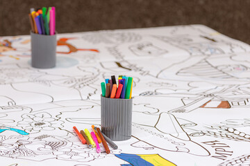Colored pencils and markers in a cup on a large coloring page with Ukrainian pictures. Colored pencils and markers. Drawing lesson. Big coloring page. Fine arts. Children's creativity. School process.