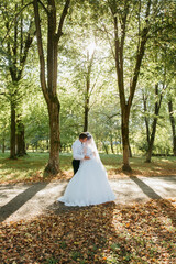 A bride and groom are standing in a forest, surrounded by trees and leaves. Scene is romantic and peaceful