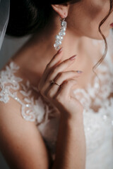 A woman is wearing a white dress and a pearl earring. She is holding her hand up to her ear