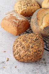 Fresh baked wheat buns with poppy,  sesame seeds closeup on metallic rack on sone table background.