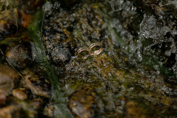 Two rings are sitting on a rock in a stream. The water is flowing and the rocks are wet